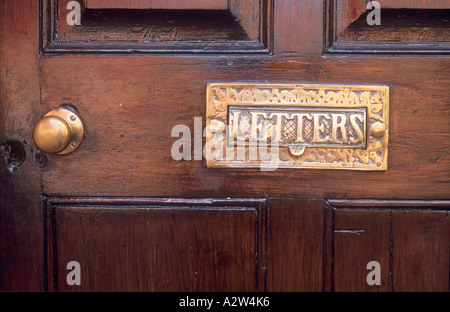 Close up di ottone ornati usurato ma è molto pulito letterbox con patta indicando le lettere impostate in marrone con pannelli colorati porta con manopola in ottone Foto Stock