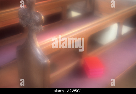 Atmosferica chiesa in legno banchi con alcuni libri rosso giacenti su un sedile bagnato dal sole Foto Stock