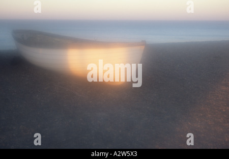 Patch atmosferica della luce del sole dorato la cattura di una barca a remi tirata su una riva di ghiaia come set di sole con mare calmo Foto Stock