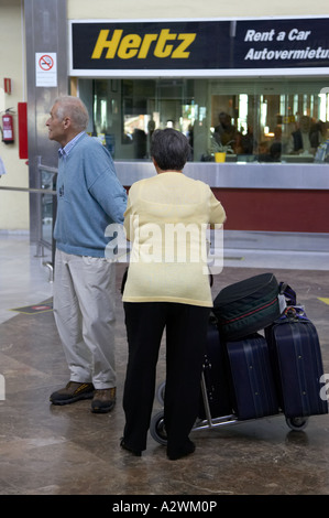 Coppia di anziani attendere con i bagagli sul carrello per bagaglio al di fuori di un autonoleggio Hertz ufficio area arrivi Reina Sofia Sur TFS Sud Airpor Foto Stock