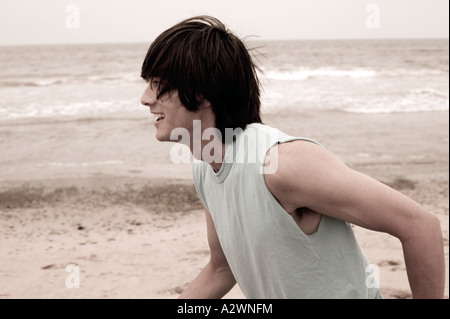 Giovane uomo che corre sulla spiaggia, sorridente Foto Stock