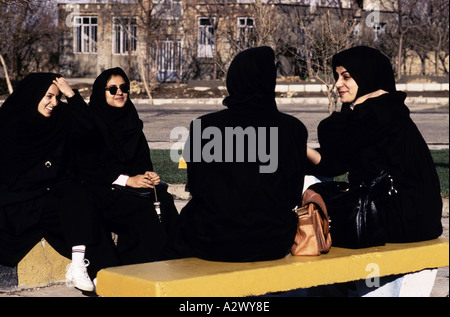 Un gruppo di quattro giovani donne sedute e parlando sul pubblico panche di via indossando islamic indossando lo chador Foto Stock