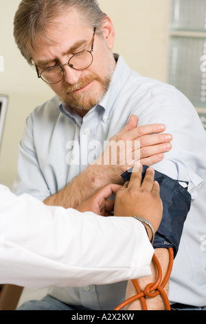 Professionista del healthcare luoghi bracciali per la pressione sanguigna sul braccio del paziente. Foto Stock