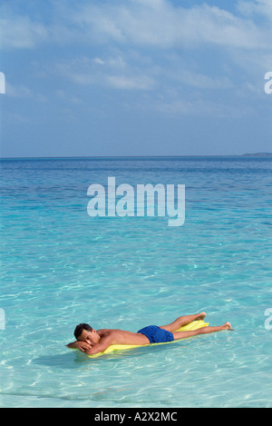 Maldive. Giovane uomo in costume da bagno sul letto aria galleggianti su acqua cristallina. Foto Stock