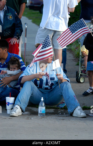 Maschio adolescente seduta sul marciapiede sventola una bandiera in una sfilata in Detroit Michigan MI Foto Stock