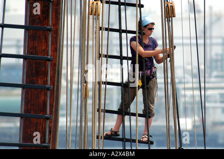 Femmina membro di equipaggio a bordo di un alto masted ship lavora ad alta fino alle manovre. Foto Stock