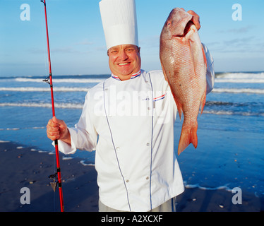 Uomo in chef's uniforme al beach tenendo il pesce appena pescato. Foto Stock