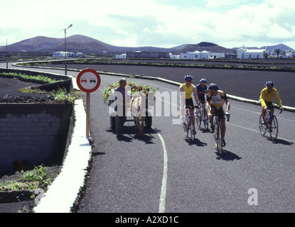 Dh CASAS DE GUIGUAN LANZAROTE ciclisti il sorpasso di uomo con asino e carrello nessun sorpasso di cartello stradale post Foto Stock