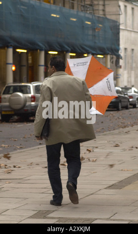 Uomo di tenere su un ombrello capovolta in forte vento Londra Foto Stock