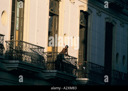 Uomo appoggiato su di un classico Balcone sul lato del classico vecchio blocco di appartamenti in città Vecchia Havana, Cuba Foto Stock