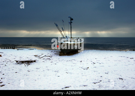 Neve su una solitaria barca da pesca a Worthing beach dopo le tempeste invernali nel Sussex e Kent in Inghilterra del Sud Foto Stock