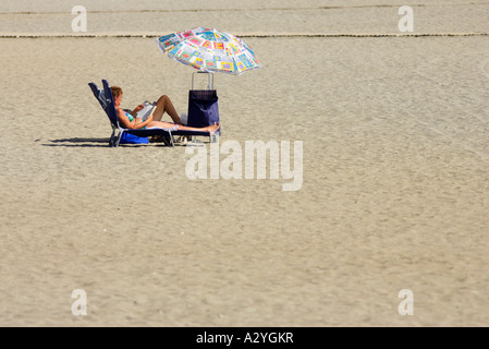 Donna sdraiata sulla sdraio con trolley e colorato ombrello ombrellino di Playa de las Americas Tenerife Isole Canarie Spagna Foto Stock