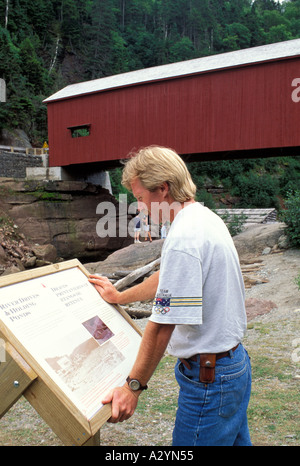 Uomo che guarda sul centro storico di marcatore in Fundy National Park con un ponte coperto in background Foto Stock