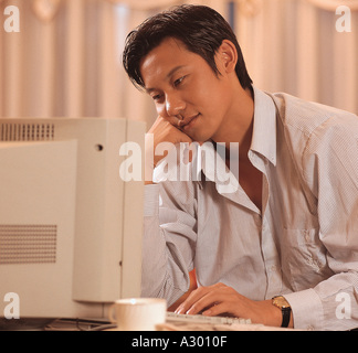 Giovane cinese seduto davanti a un computer pensando Foto Stock