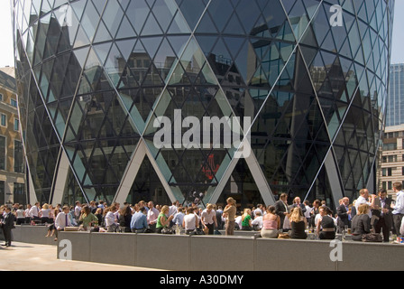 Città di Londra vicino alla base dell'edificio Gherkin con impiegati all'aperto che lavorano all'ora di pranzo in un caldo giorno estivo Inghilterra Regno Unito Foto Stock