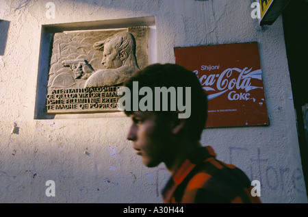 Un ragazzo cammina passato un murale socialista e capitalista un annuncio pubblicitario per la Coca Cola su una parete a Tirana in Albania Foto Stock