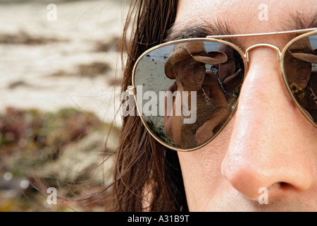 Vista di un womans riflessione su un giovane mans occhiali da sole. Foto Stock