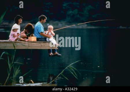 Famiglia con due figli e un cane avente un picnic e pesca dal molo Foto Stock