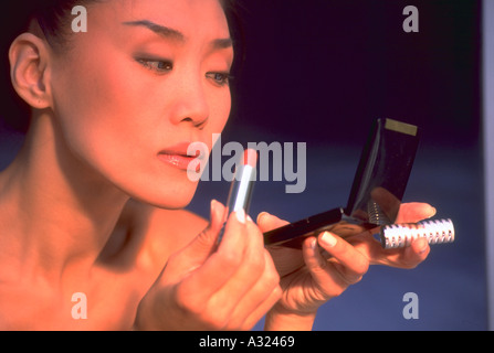 In prossimità di una donna asiatica utilizzando uno specchio compatto e il rossetto Foto Stock