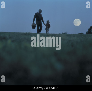 Padre e figlia camminando mano nella mano in un campo al chiaro di luna Foto Stock