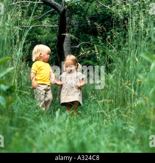 Piccolo Ragazzo e ragazza tenendo le mani come camminano insieme attraverso un alto campo erboso Foto Stock