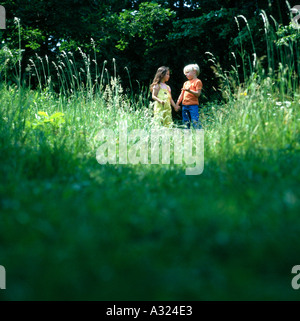 Ragazzo e ragazza tenendo le mani come essi a piedi attraverso un alto campo erboso Foto Stock