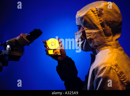 Un tecnico elettronico indossando indumenti di protezione tenendo un piccolo disco rigido in un elettronica stanza pulita Foto Stock