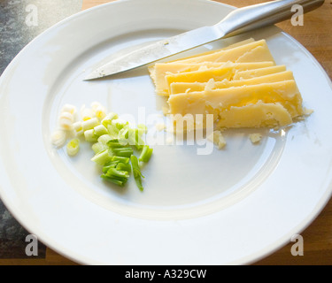 Agriturismo mature cheddar e cipolline tagliate su una piastra con un coltello Foto Stock