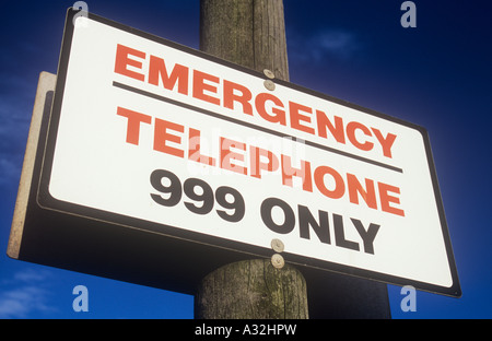 Bianco rosso e nero segno su un palo telefonico contro profondo cielo blu indicante che il telefono di emergenza solo 999 Foto Stock