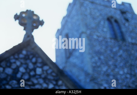 Vista atmosferica dal di sotto della pietra crocifisso sul vertice del portico della chiesa con quadrato campanile merlato dietro e cielo bianco Foto Stock