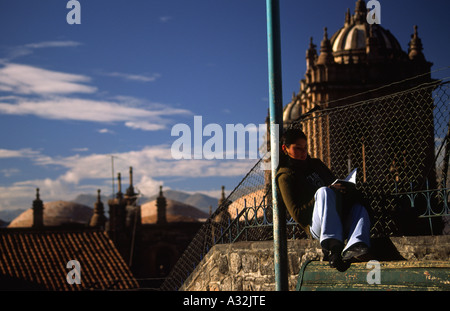 Ragazza adolescente studente la lettura di un libro in un Cusco street nella parte anteriore della tipica architettura, Perù, Sud America Foto Stock