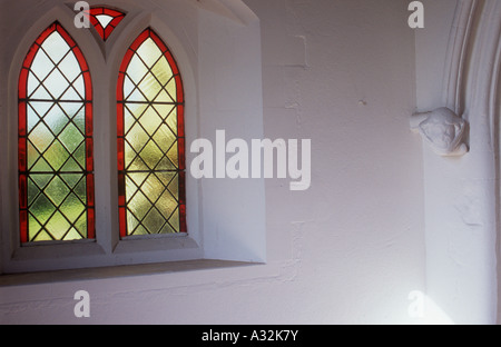 Interno del portico della chiesa nella luce calda con red-frange diamante windows con piombo e indossato scolpiti corbel medievale di testa di donna Foto Stock