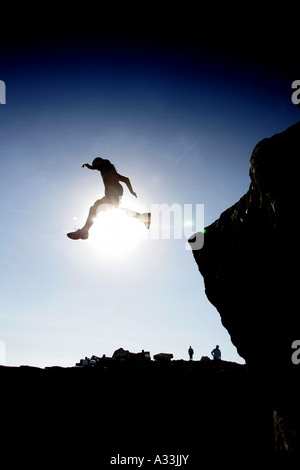Persone salta fuori ,tombstoning, off portland bill in silhouette della Sun per il divertimento in mare sotto la guardato da curiosi Foto Stock