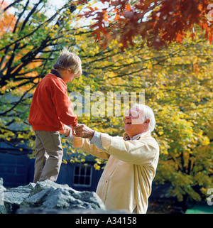 Un sorridente nonno tiene il suo nipote con le mani in mano mentre il bambino si arrampica su di una roccia in autunno Foto Stock