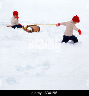 Un giovane bambino tirando un altro bambino su una pista da slittino slitta tipo attraverso la neve Foto Stock