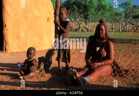 Himba tribù Ovahimba donna con bambini seduti davanti al rifugio Kraal interno Kaokoveld Namibia Africa Foto Stock