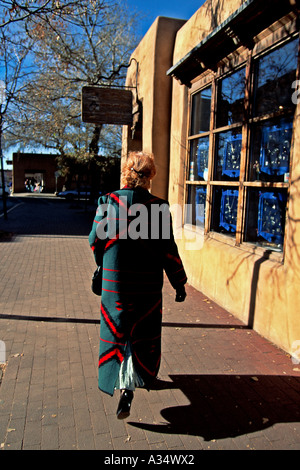 Donna che indossa lungo cappotto di lana con pattern southwestern passeggiate sul marciapiede di mattoni nella zona della Città Vecchia, Santa Fe, New Mexico Foto Stock