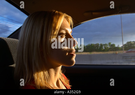 Donna bionda in sella passeggero in un'auto. Udienza con il profilo rivolto allo spettatore la faccia è illuminato dal sole al tramonto. Foto Stock