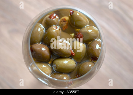 Green Olive ripiene con pomodori secchi in un bicchiere di olio di semi di girasole Foto Stock