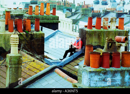 Sul tetto di un artista disegna un paesaggio urbano tra le lastre di ardesia e piastrelle. Foto Stock