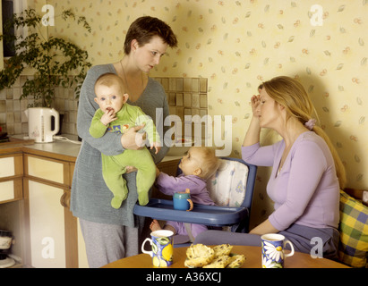 Premuto cercando la madre con un bambino ascolta mentre un altro madre parla con lei in cucina Foto Stock