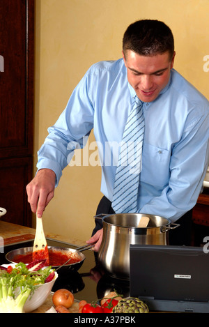 Mann beim kochen in der Kueche, Uomo in camicia e cravatta in cucina durante la cottura per la cottura della ricetta in computer notebook Foto Stock