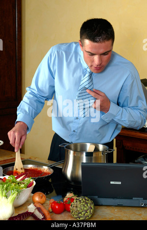 Mann beim kochen in der Kueche, Uomo in camicia e cravatta in cucina durante la cottura per la cottura della ricetta in computer notebook Foto Stock