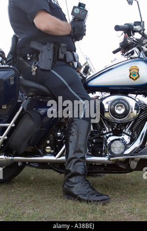 Vista laterale di un poliziotto in uniforme della motocicletta seduto sulla sua moto con un dispositivo di misurazione della velocità nelle sue mani funzionario di polizia astratto Foto Stock