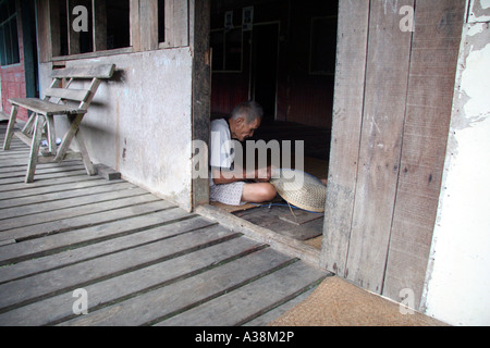 Vecchio Iban headhunter tessitura di un cestello di rattan nella sua longhouse sulle rive del Sungai Terika, Sarawak, Borneo, Malaysia Foto Stock