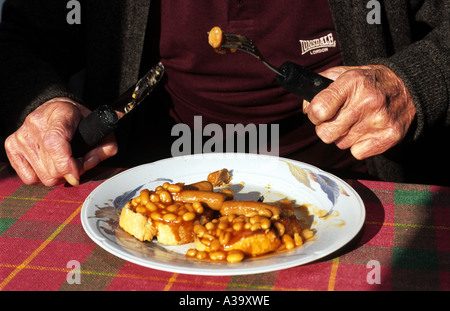 Vecchia età titolare di pensione o di rendita di mangiare una colazione a base di fagioli su pane tostato nella sua casa di Suffolk, Regno Unito. Foto Stock