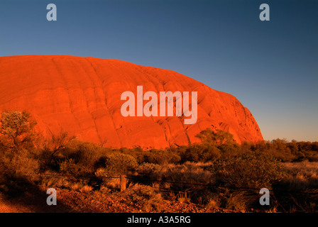 Drammatica e vista diversa di Ayers Rock poco dopo l'alba come visto lungo la base a piedi intorno a Uluru rosso bagliore arancione incandescente Foto Stock