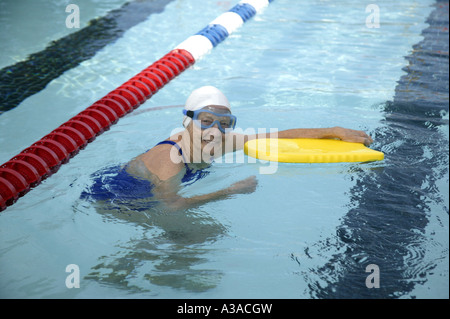 Senior donna utilizzando kickboard, piscina esterna Foto Stock