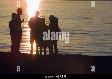 Un gruppo di giovani amici radunati sulla spiaggia a guardare il tramonto Foto Stock