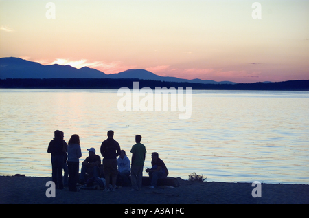 Un gruppo di giovani amici radunati sulla spiaggia a guardare il tramonto sul Puget Sound Foto Stock